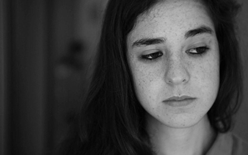 A contemplative young woman with acne highlighting the link between hair care products and skin breakouts.