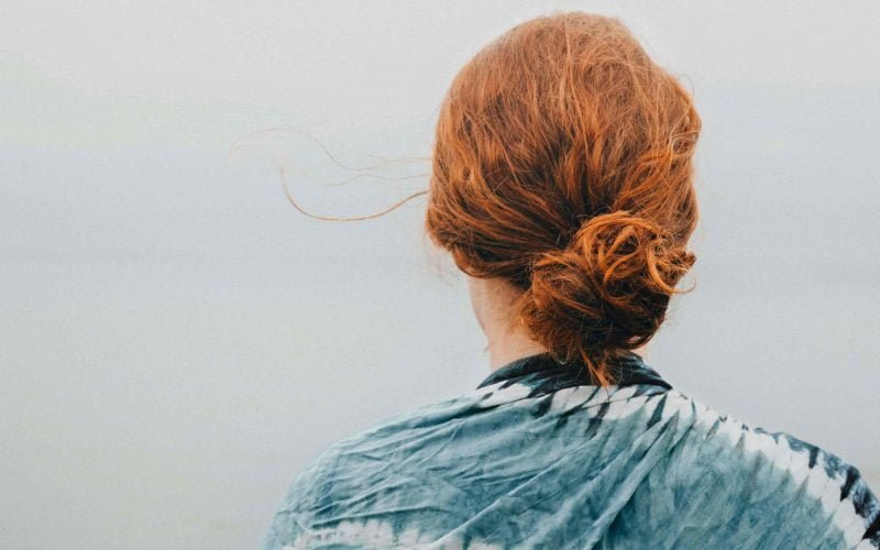 Back view of a woman with dry, red hair tied up, symbolizing the need for proper hair care.