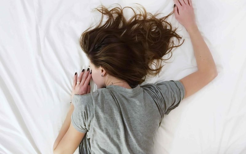 Woman lying on a bed with her hair spread out, illustrating the best hair care for sensitive scalps.