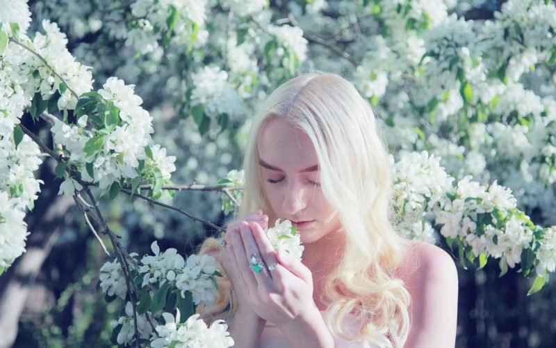 Woman in a lush garden, smelling white blossoms, embodying the essence of serenity and beauty, perfect for illustrating articles on skin care and nature's impact on wellness.